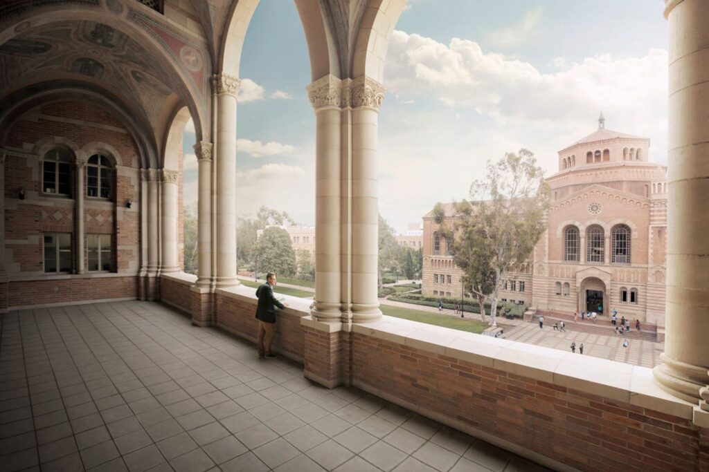 A man stands inside the Royce Hall loggia, overlooking Dickson Quad and Powell Library. 